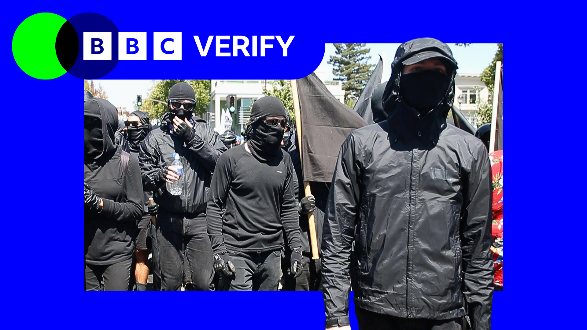 A group of people dressed in all-black, with their eyes and mouths covered by sunglasses and masks, march forward during an anti-fascist protest