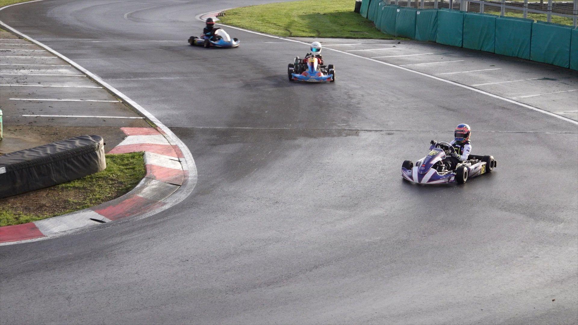 Three karts and drivers can be seen entering a corner at a race circuit.