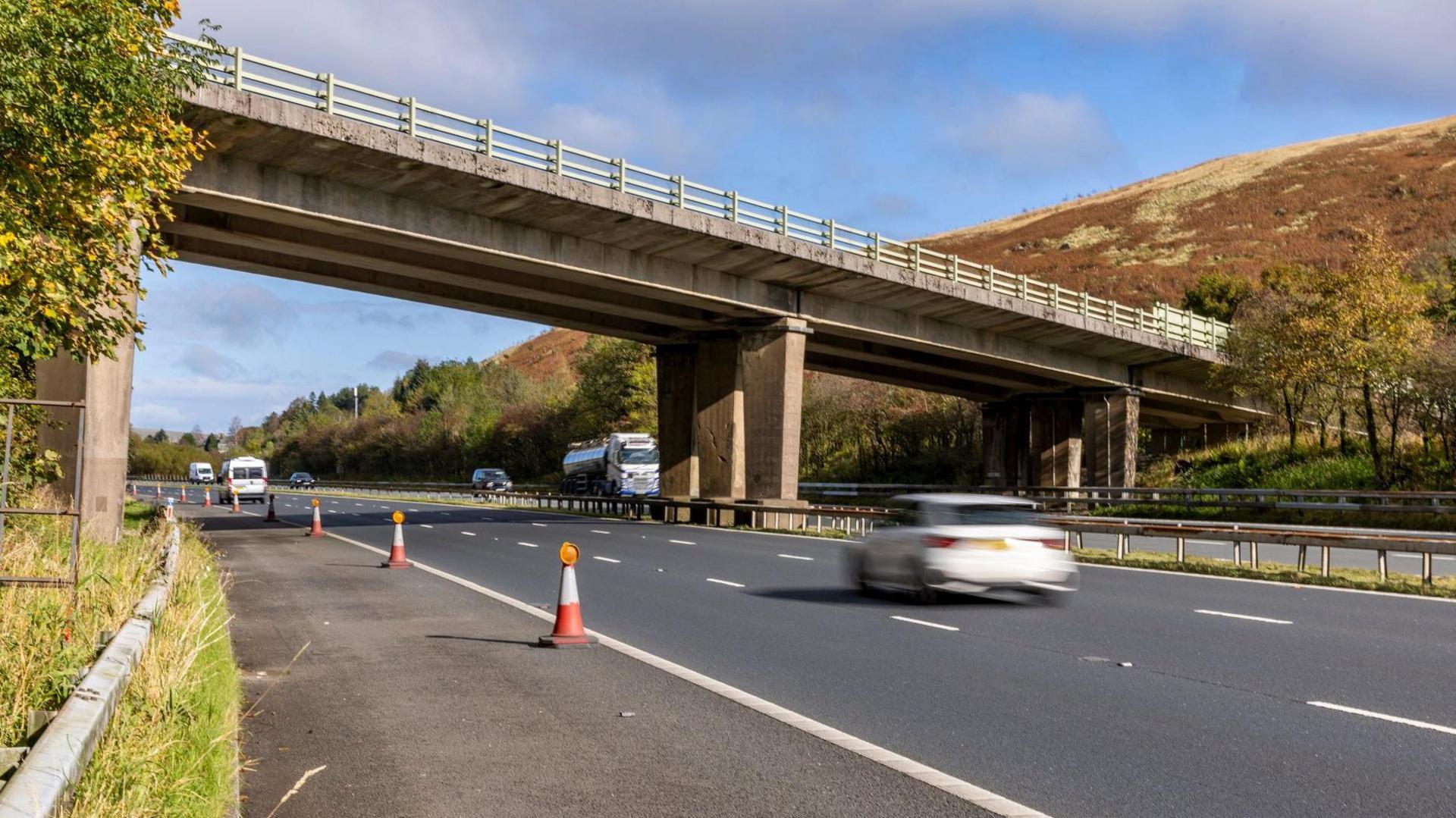 The M6 going through the Lune Gorge by the Lawtland House Bridge near Tebay, Cumbria, looking northbound between junctions 37 and 38. Cars and lorries are pictured travelling on the motorway during a sunny early Autumn day with green hills and blue skies in the background.
