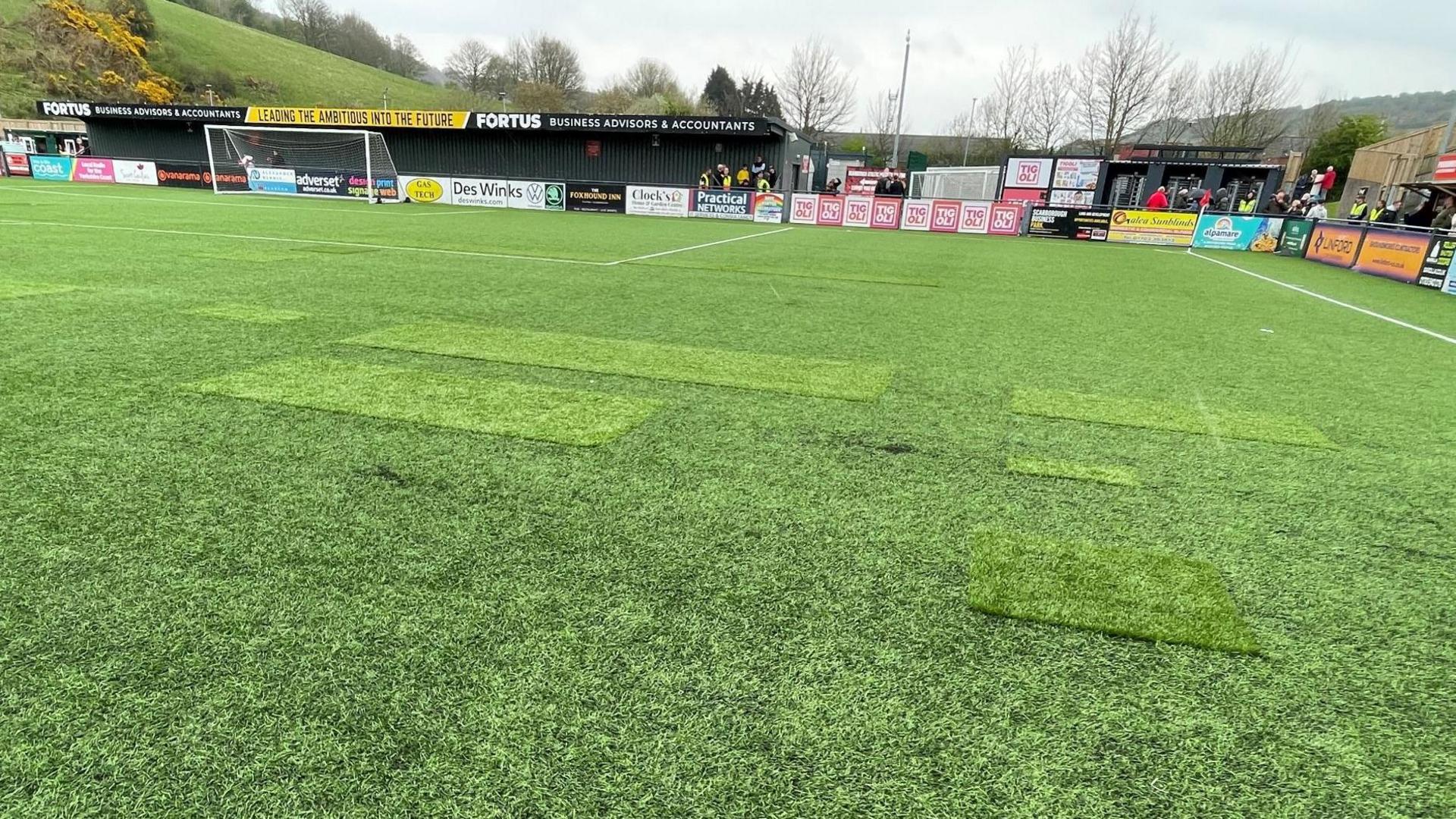 A football pitch with patches where parts have torn or created holes.