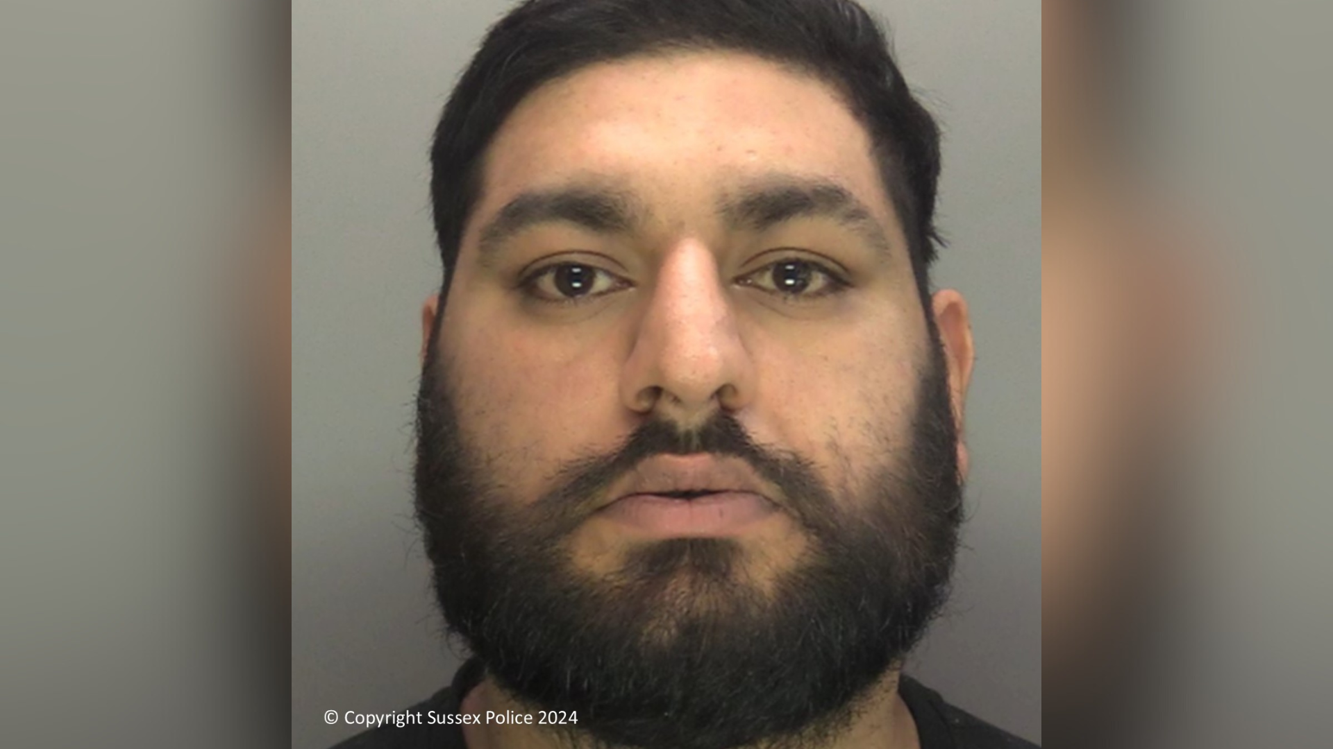 A police custody photo of a man. The man has short black hair and a black beard.