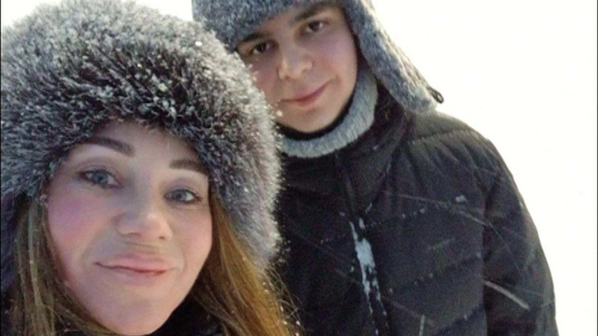 A close-up of a woman and a young teenager, both wearing fur hats amid a snowstorm