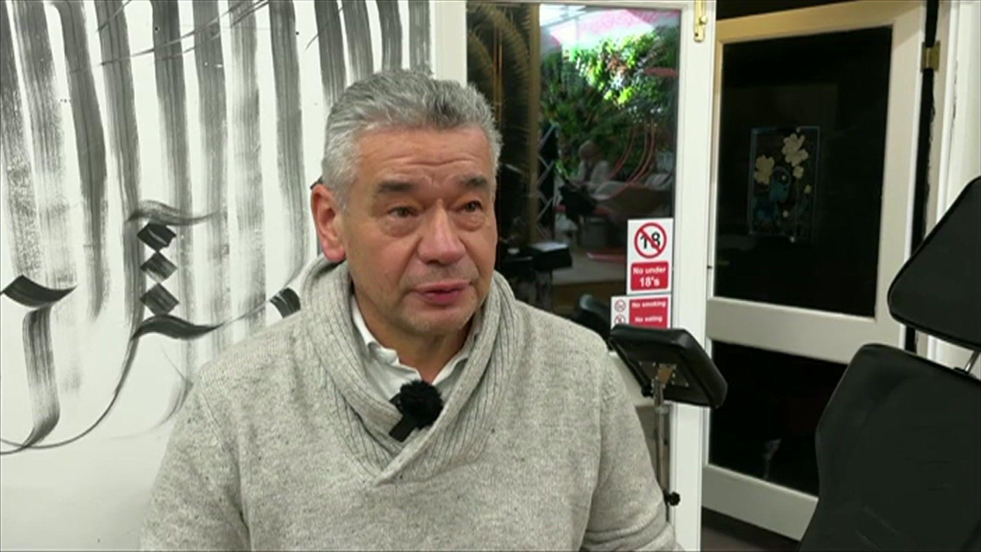 Tim Oglethorpe in a grey jumper and white shirt in a shop with a black and white wall and open door.