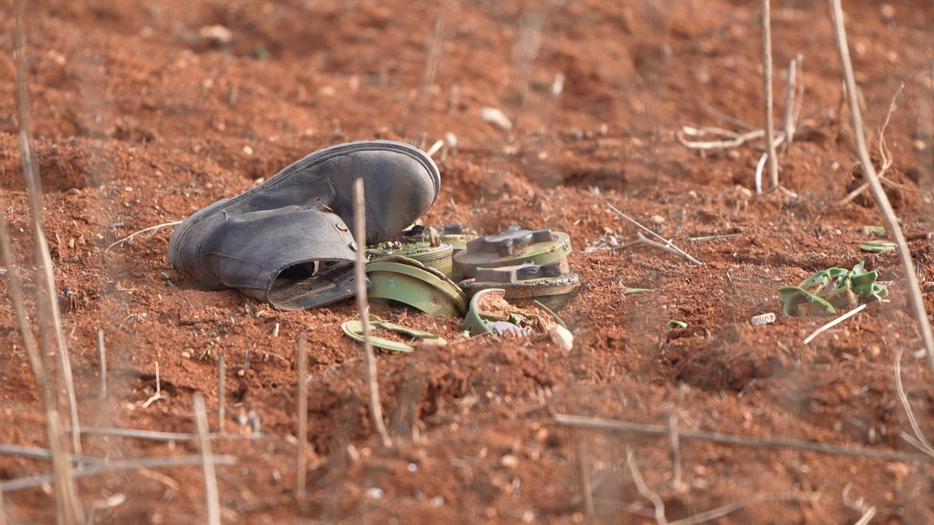 Male black boot laid next to cluster of green landmines