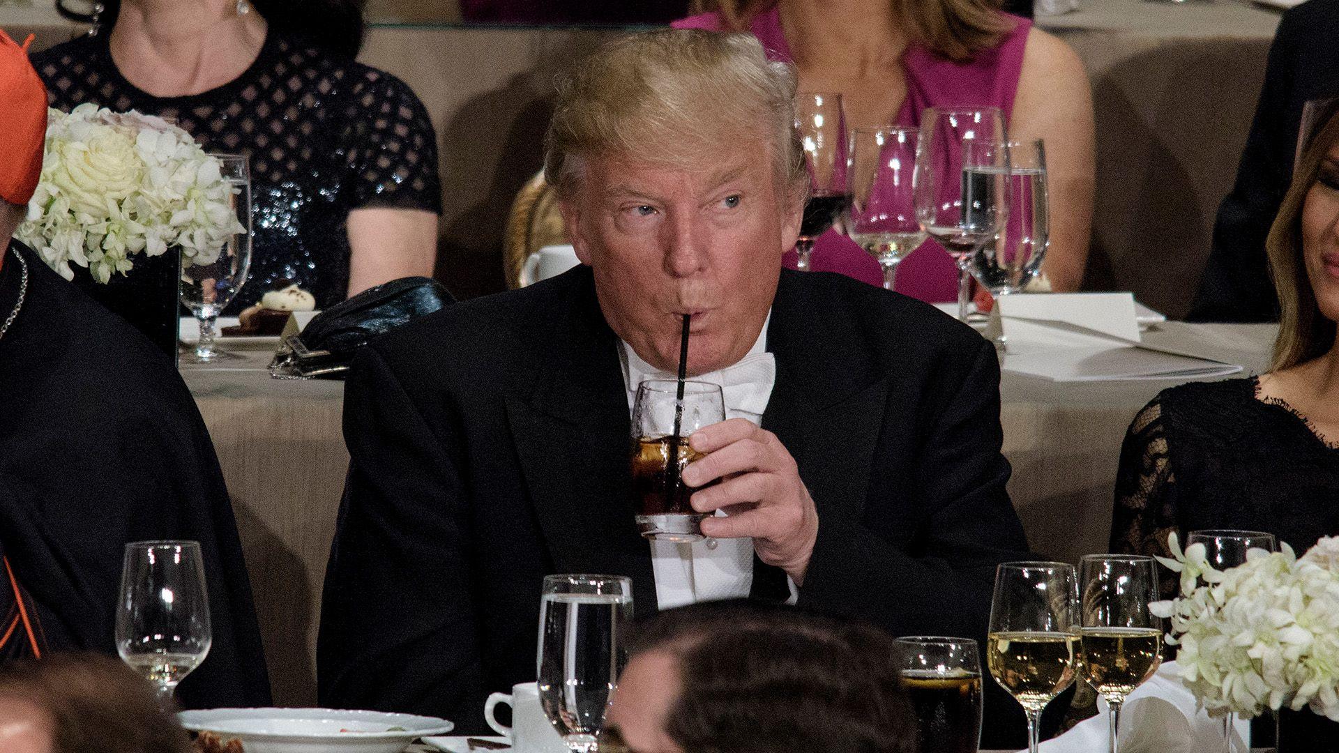 Donald Trump drinking out of a straw at a dinner