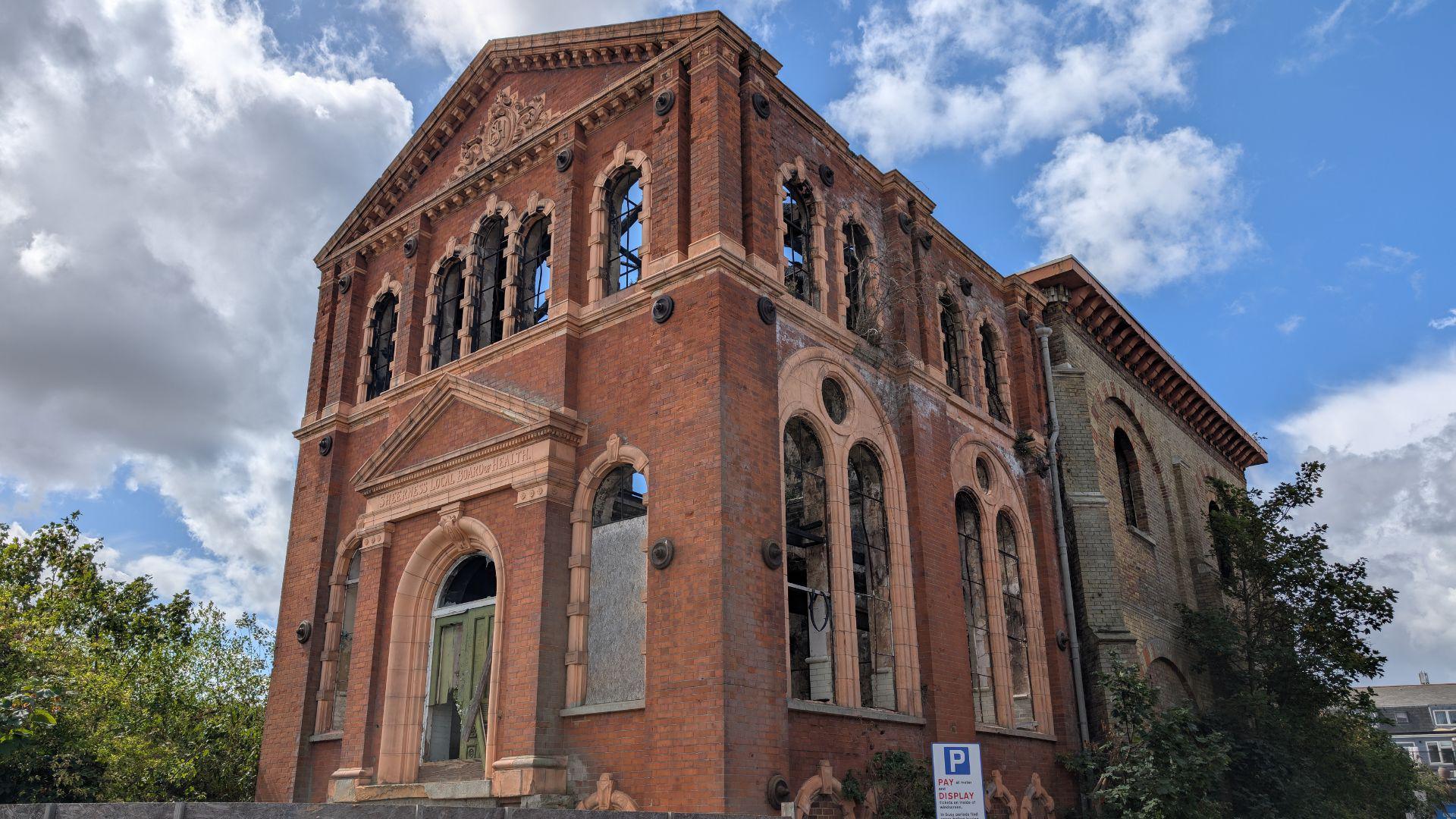 A large brick building with arched windows. The building's roof and windows are missing, there are some scorch marks on the brickwork