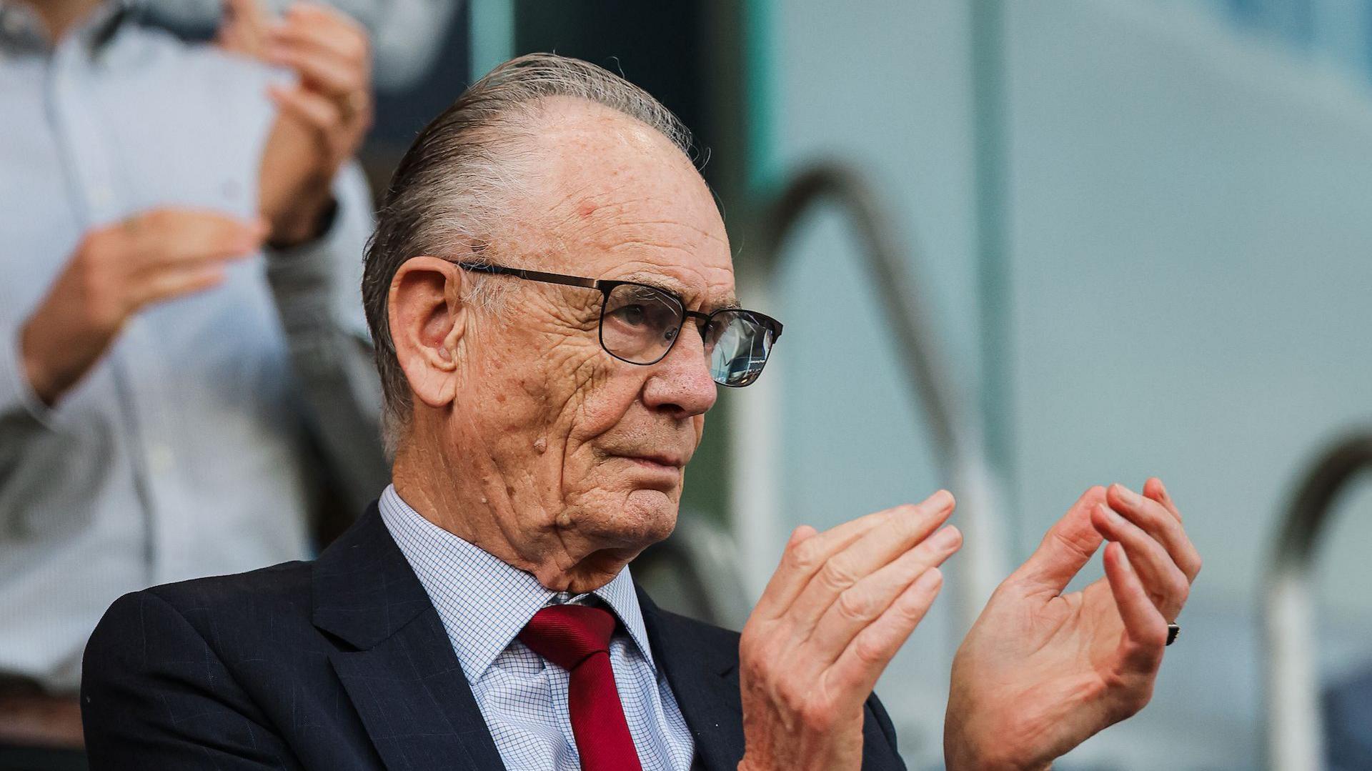 Ken Davy clapping his team, while wearing a navy suit with a crimson tie 