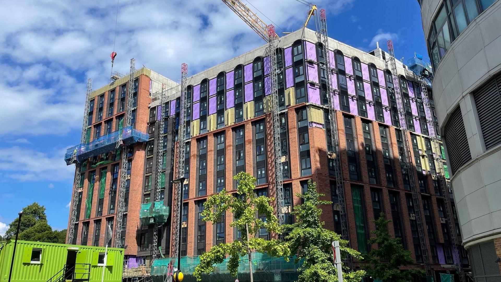 A partially-built student accommodation block is surrounded by cranes