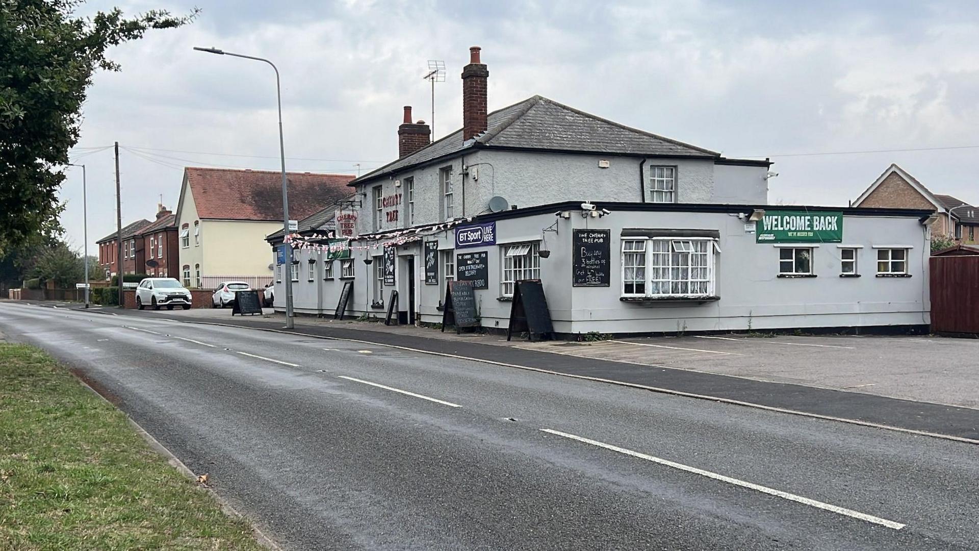 The road outside the Cherry Tree pub, which is a grey and black building with a small car park to its side.