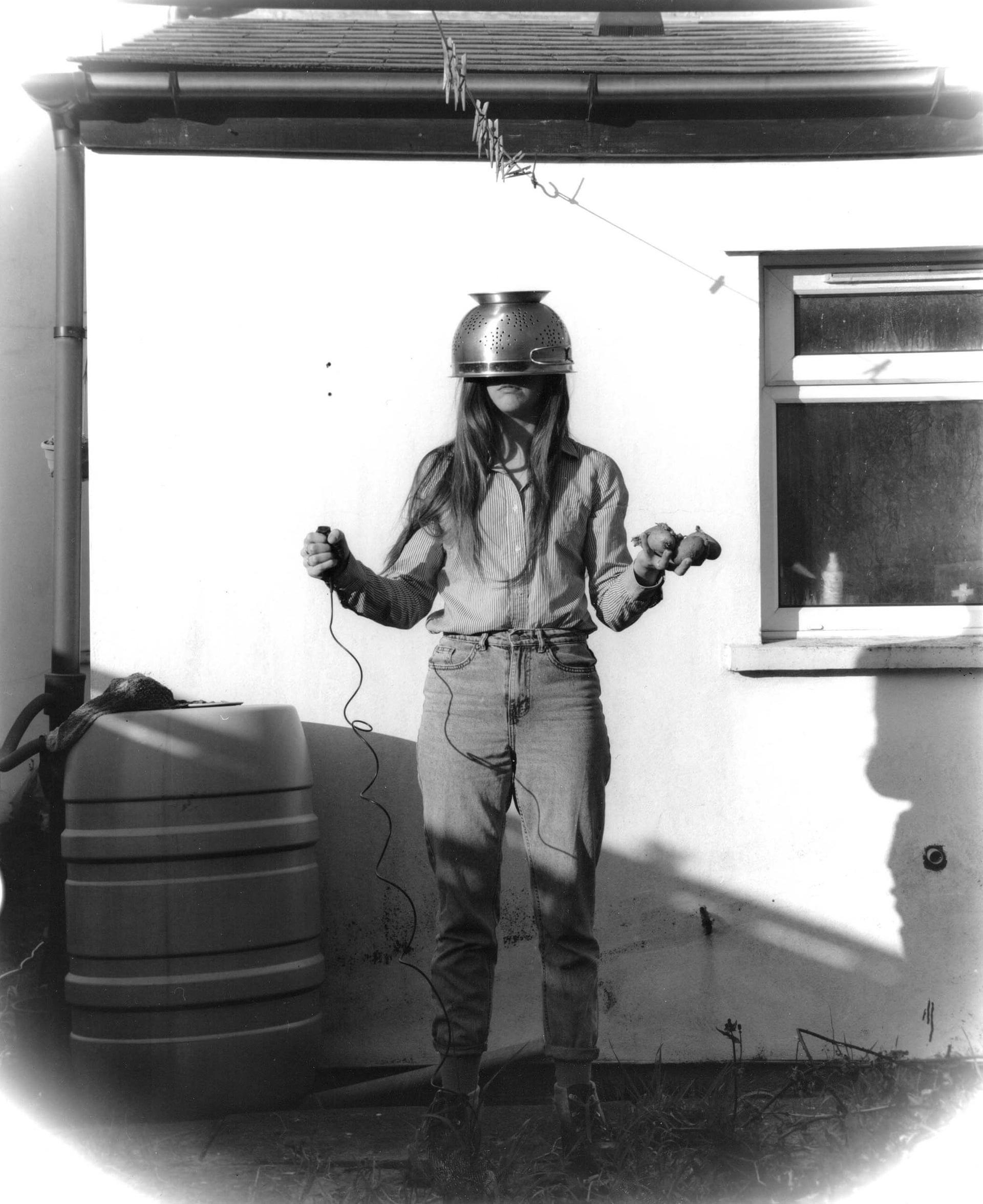 woman-stood-with-colander-on-her-head-holding-potatoes