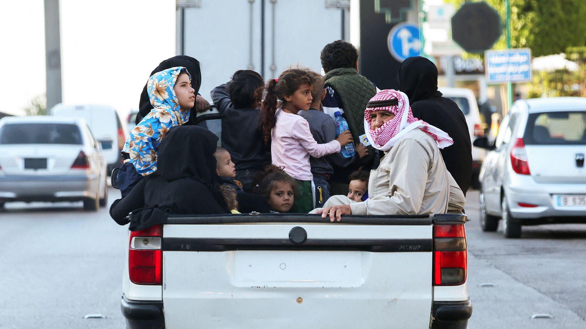 a group of children and adults squeezed into the back of a truck driving through beirut