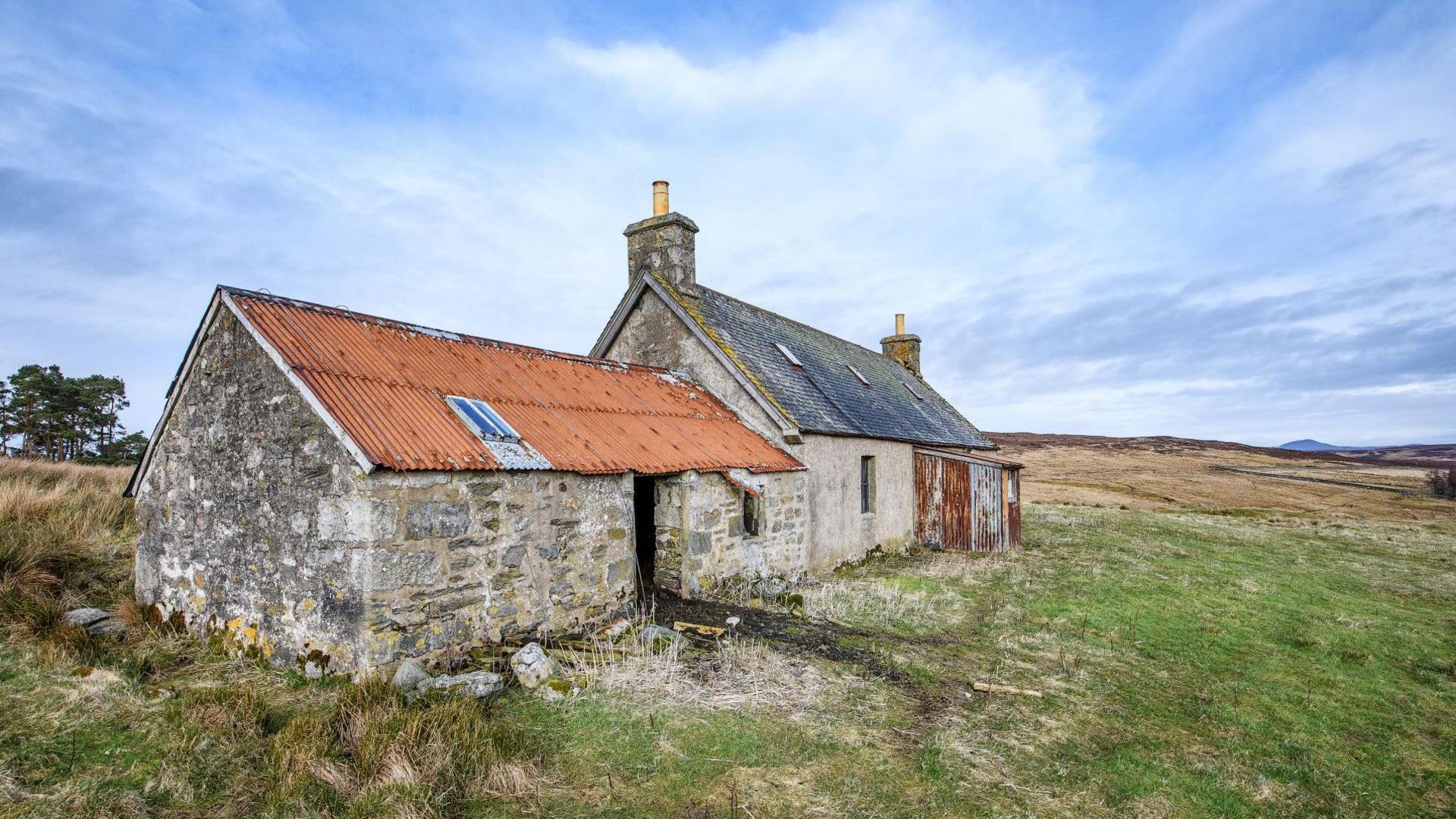 The single-storey house has an outbuilding attached to it. The property is in a rural Highland setting of wide open fields.