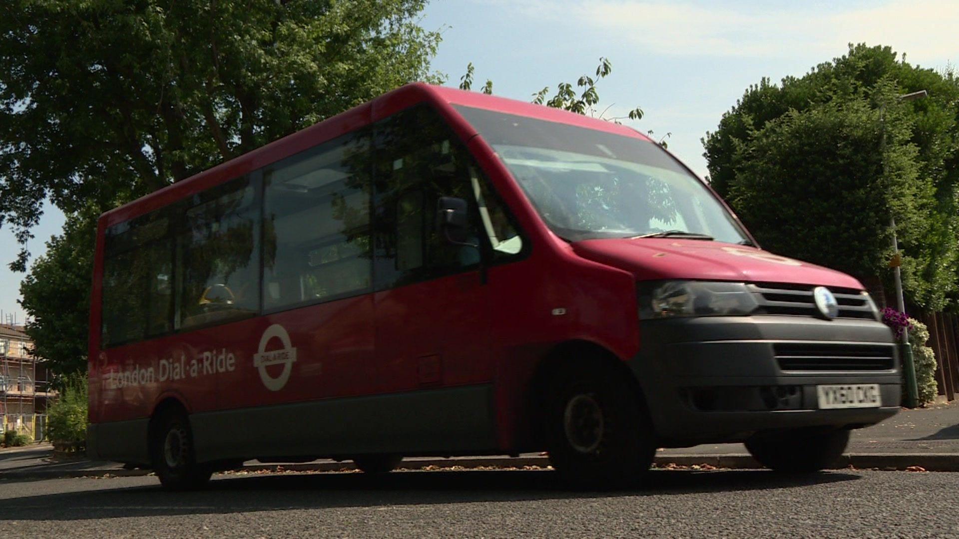 A red Dial a ride minibus driving on the road with trees in the background