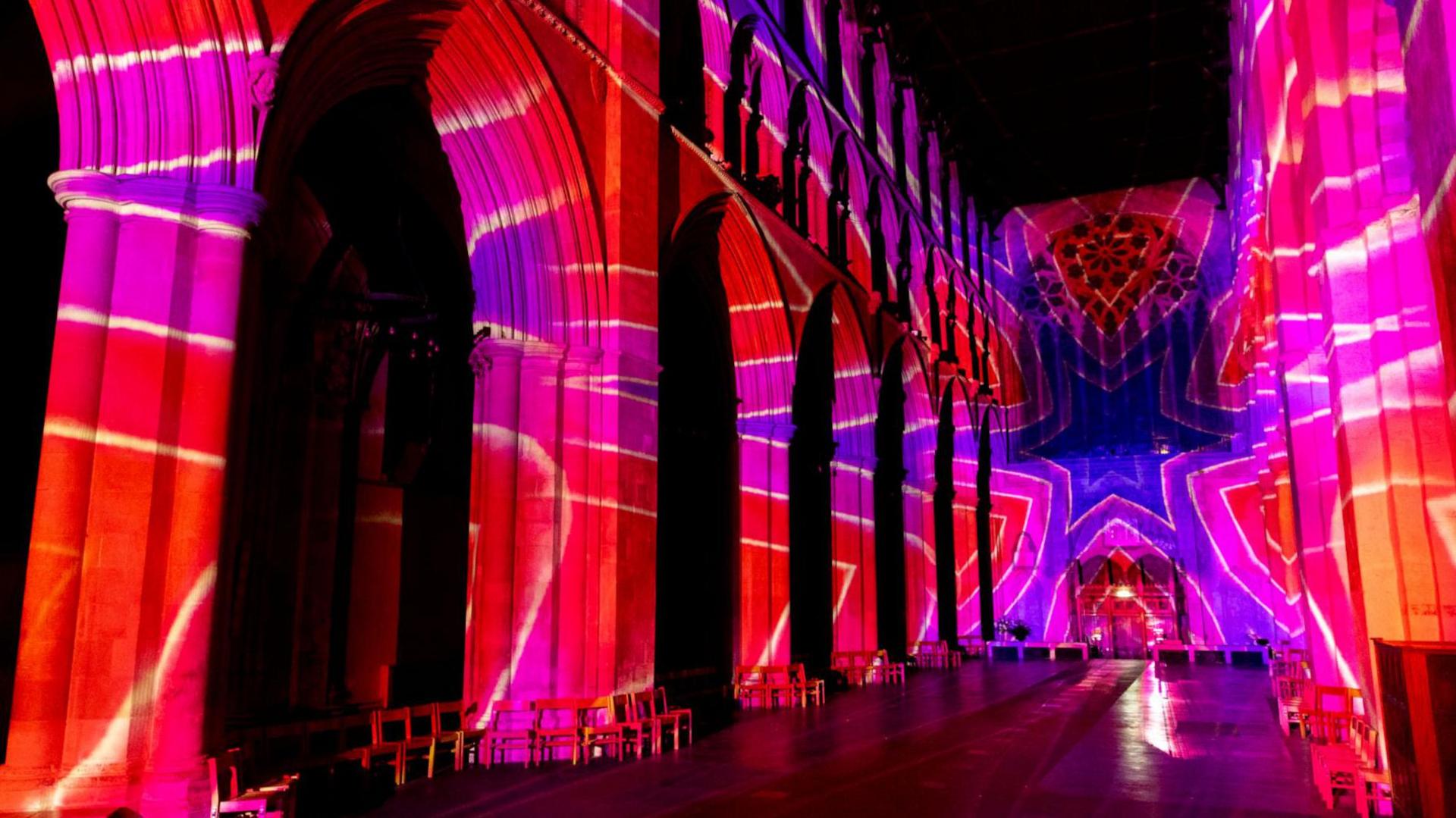 Larger poppy shapes in red, pink and purple are projected on to the walls and ceiling of the nave of St Albans Cathedral.