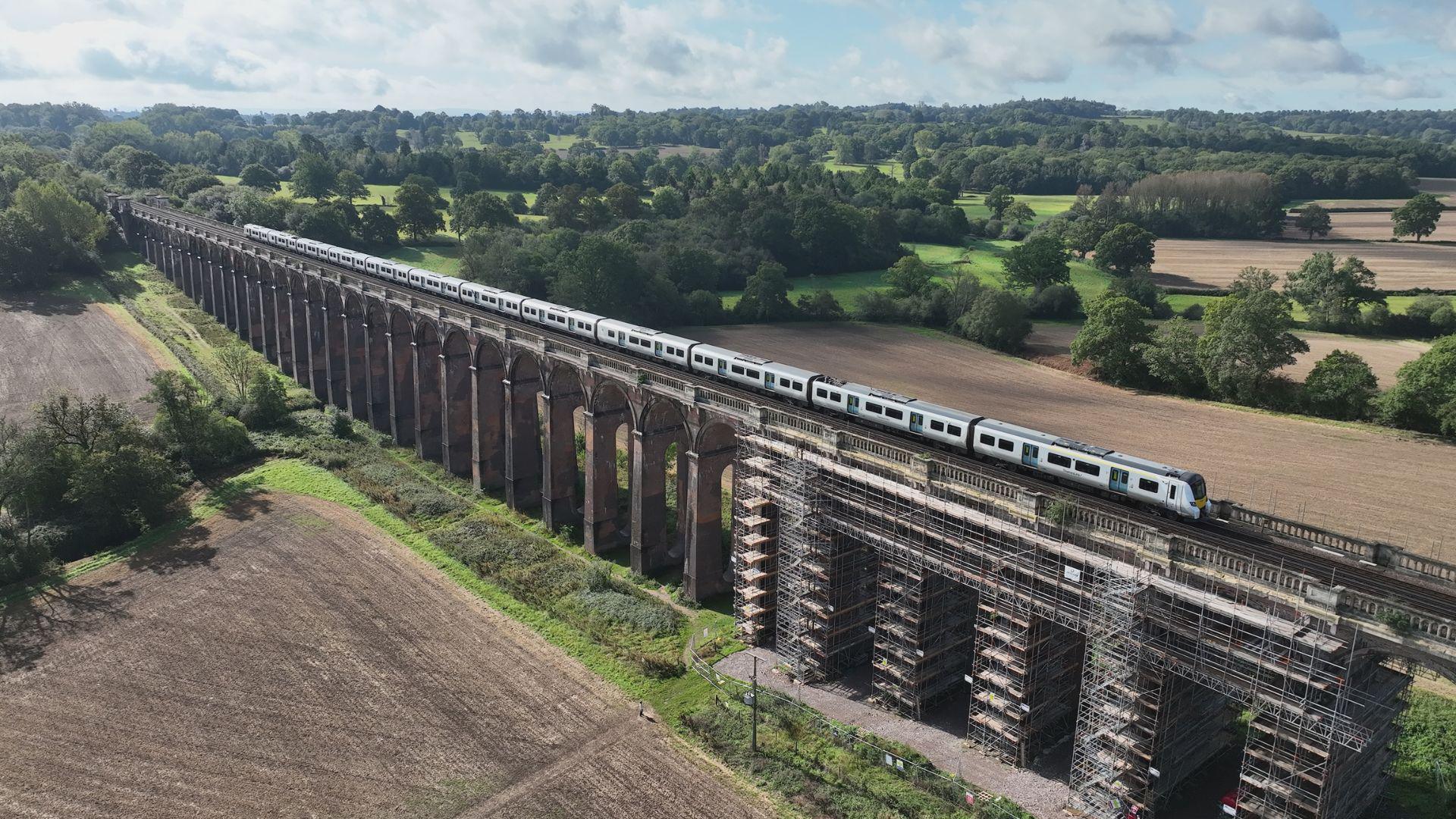 A train going across the Ouse Valley viaduct. There are trees and fields below