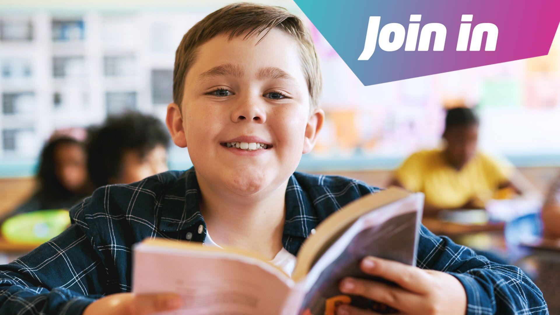 A child holds a book and smiles in the classroom
