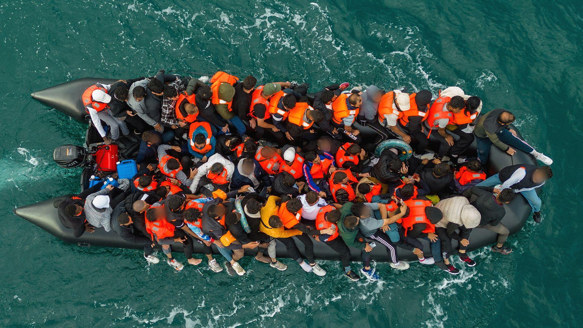 An aerial view of an inflatable dinghy overcrowded with migrants, motoring through the sea.