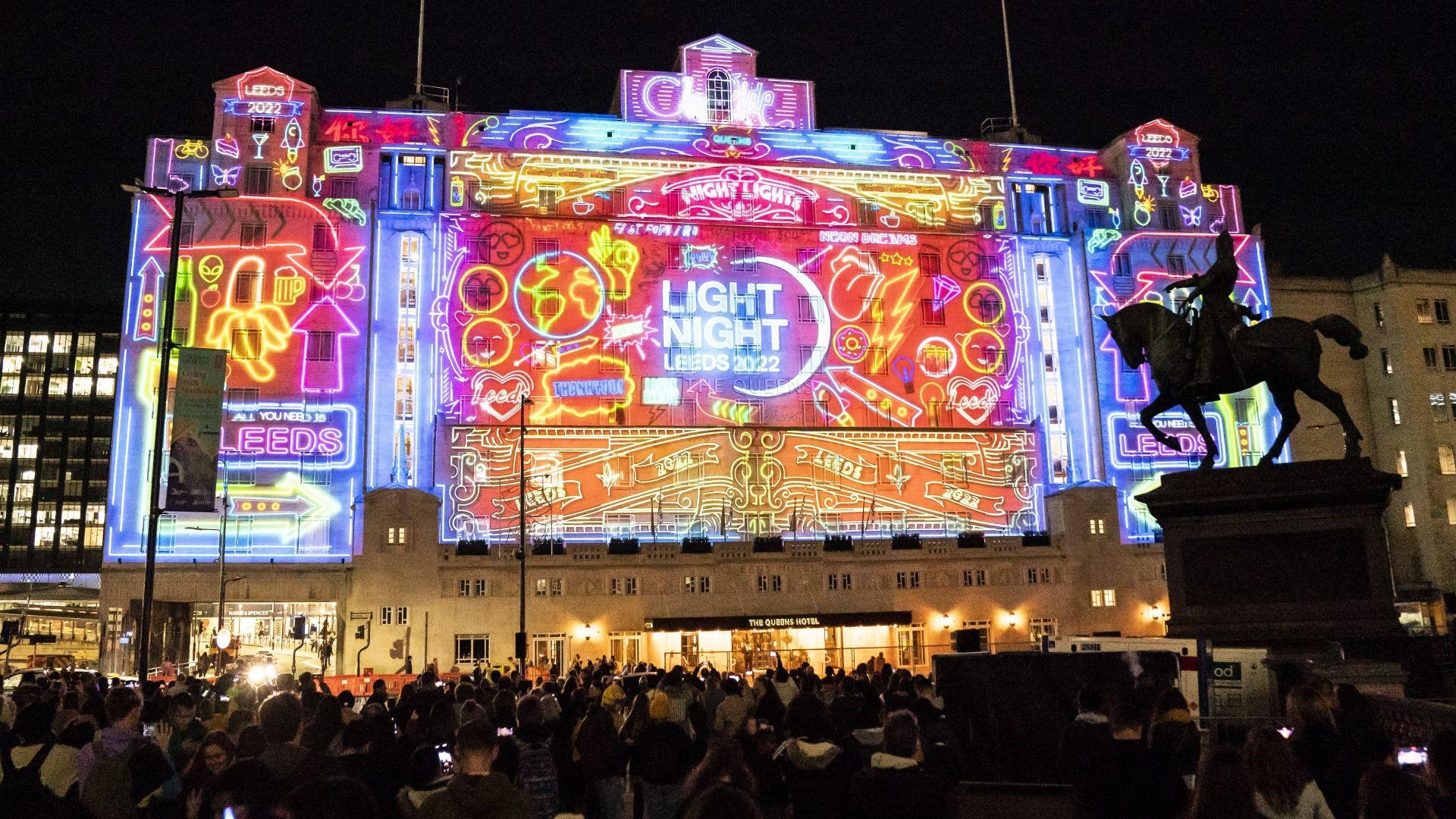 Colourful lights and patterns are projected on to the side of a large hotel in Leeds. In the centre of the building the words Light Night Leeds 2002can bee seen in a bright blue light.