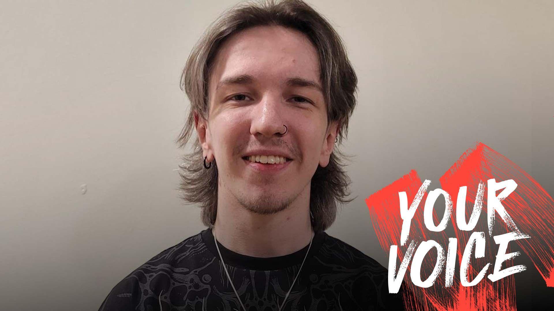 Liam Davidson with blonde hair wearing a black t shirt with a grey pattern a silver necklace and a black nose ring and earring smiling at the camera with the graphic Your Voice