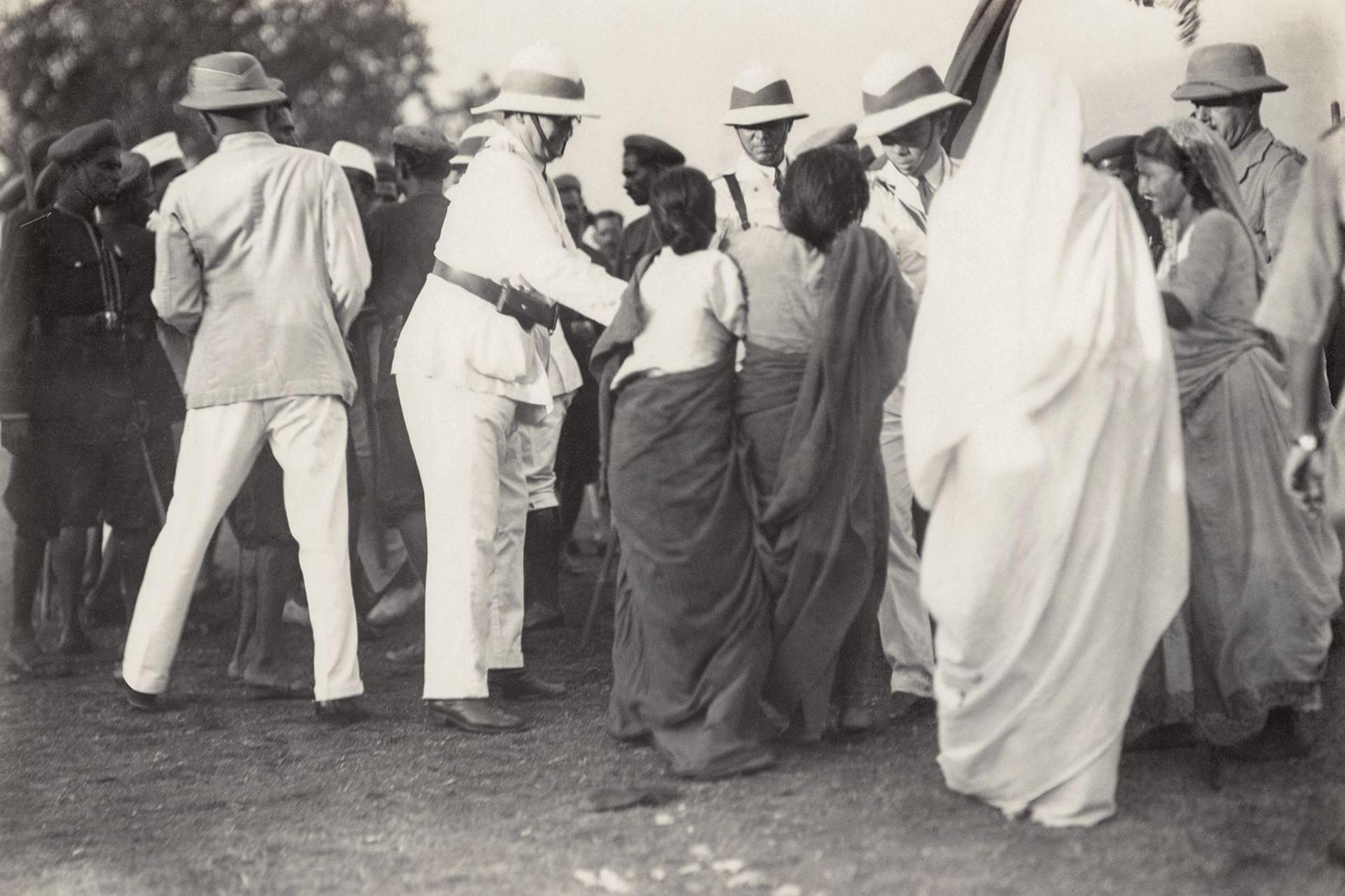Two women, who are members of a women's volunteer force and are dressed in saris, struggle with police officers as they try to seize their provisional national flag