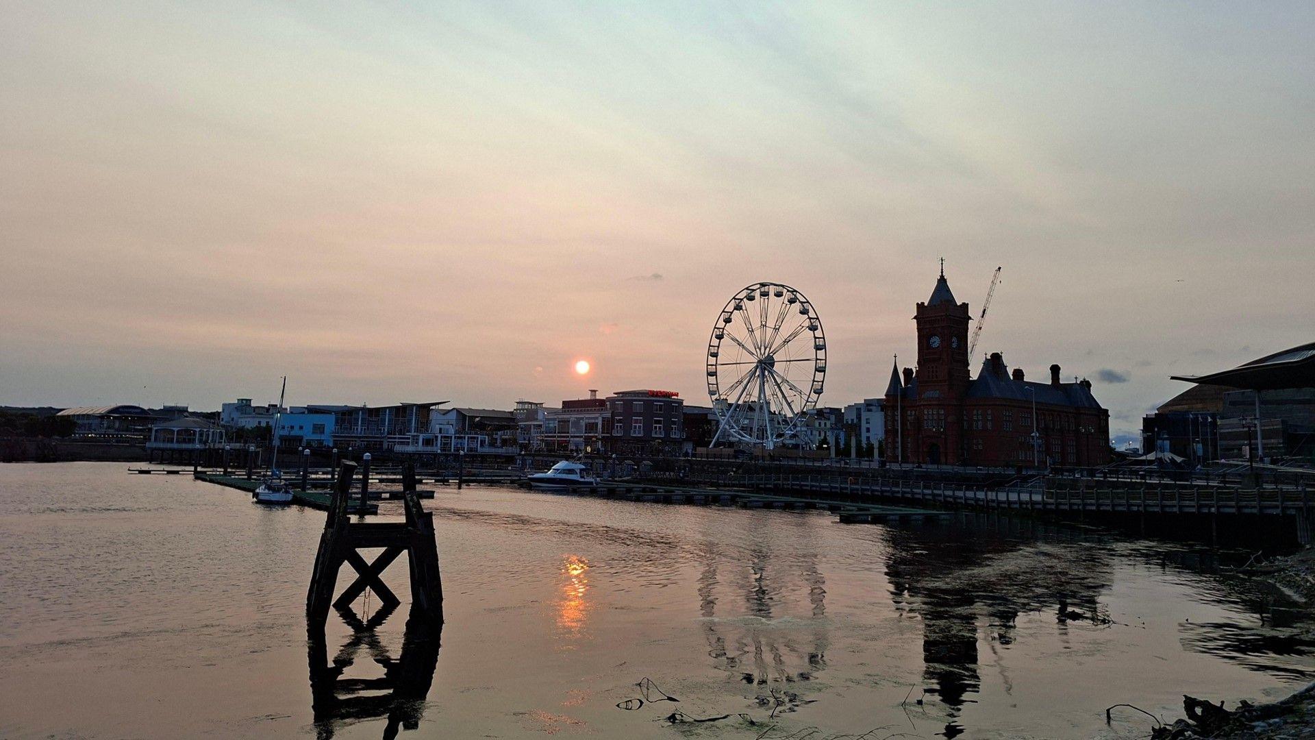 Cardiff Bay and buildings in front of a dirty coloured sky and disc of a setting sun.