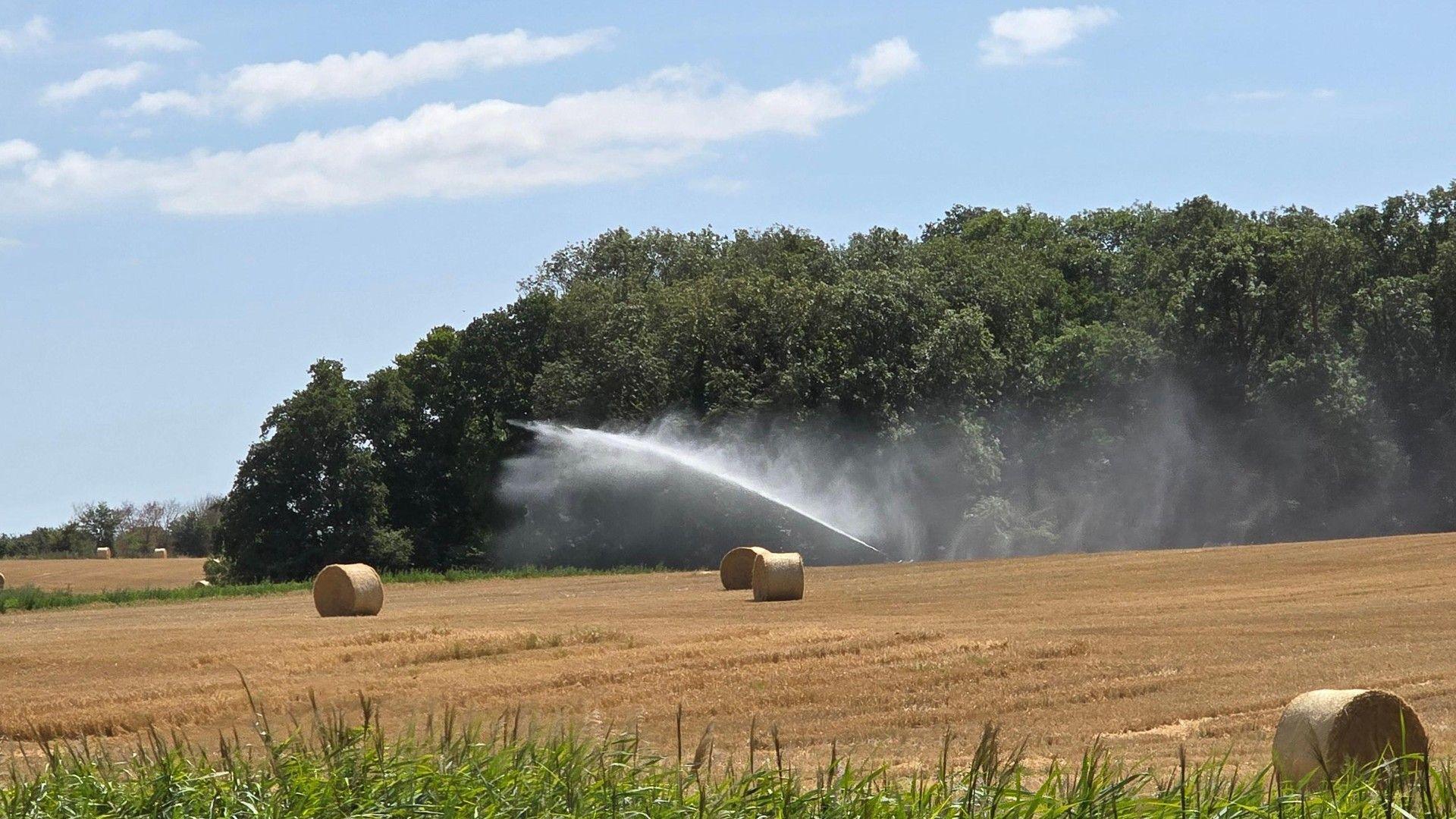 Hay bales in a field and an agricultural hose sprays in the background