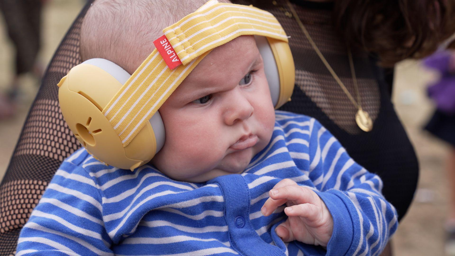 A baby wearing yellow ear defenders and stripy blue pyjamas at Glastonbury