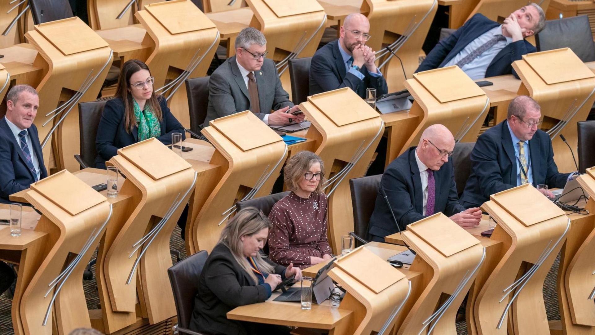 Two rows of politicians sitting in the SNP seats in the Holyrood chamber, including Audrey Nicoll, John Swinney, Kate Forbes and Michael Matheson 