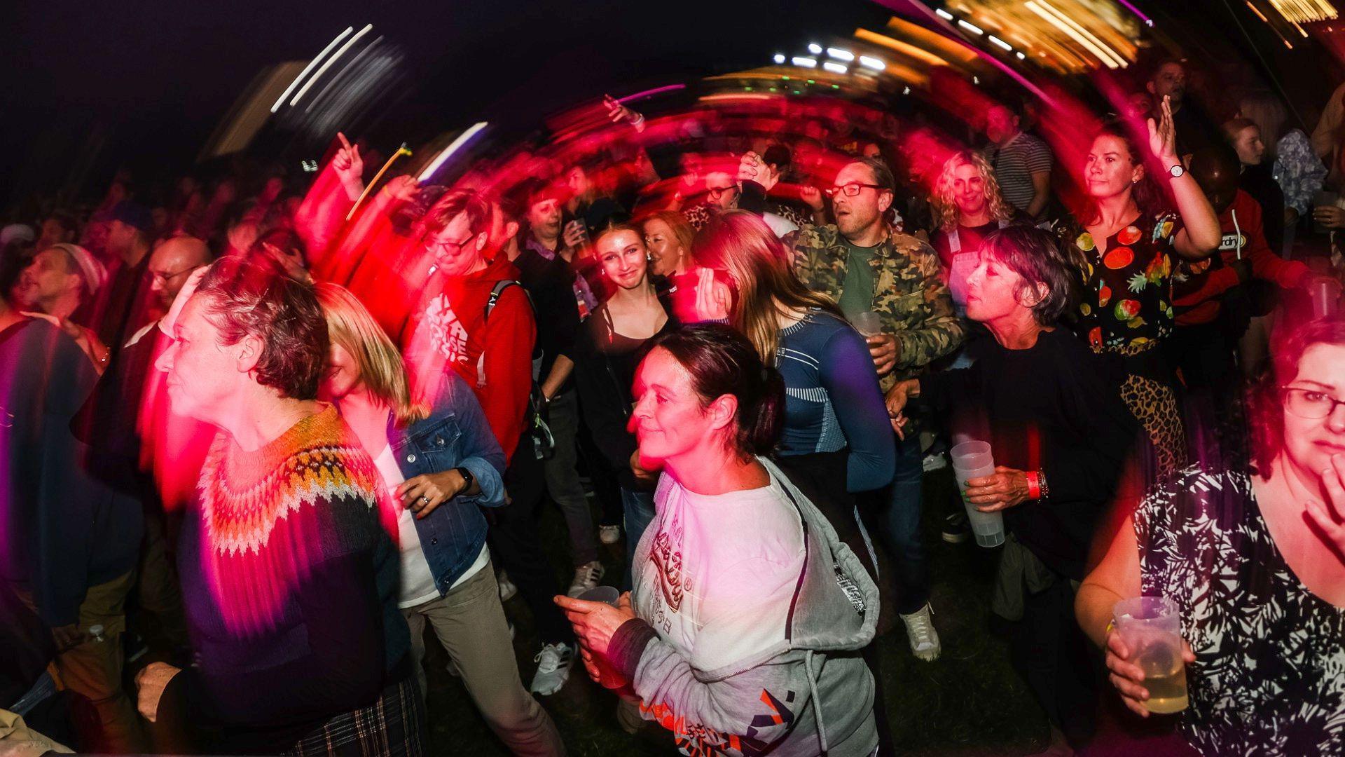 A crowd of people at the event, there is an artistic effect on the image to make it looks like it's swerving round in a circle, people are looking towards the stage, dancing or socialising with friends