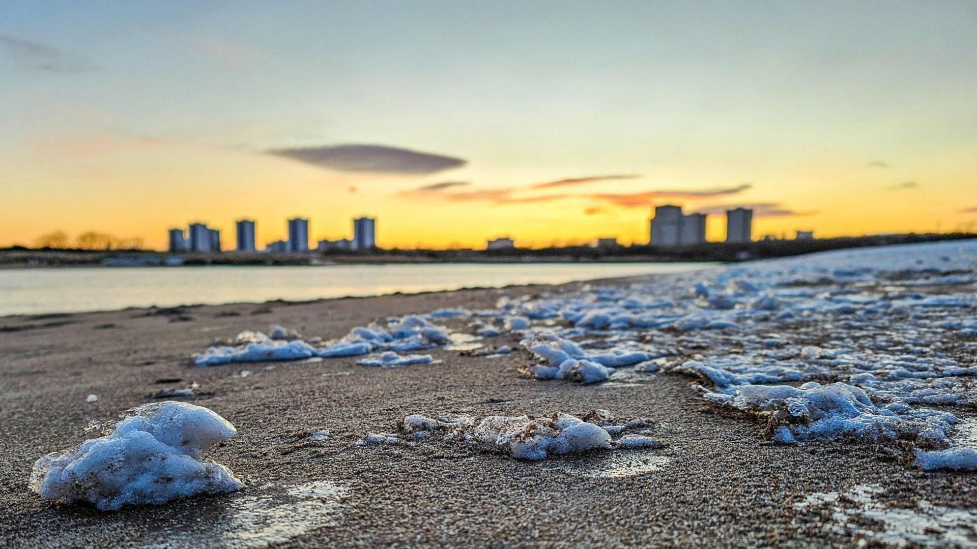 The frozen chunks cover the sand on a beach near Aberdeen. The city's tower blocks are almost silhouetted against a yellow sky. 