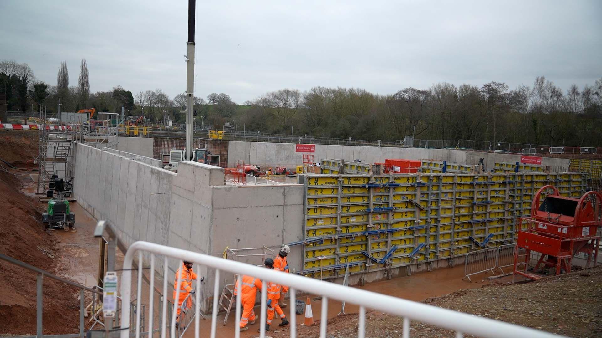 A construction site, with the installation of large concrete pool located in the centre well under way.