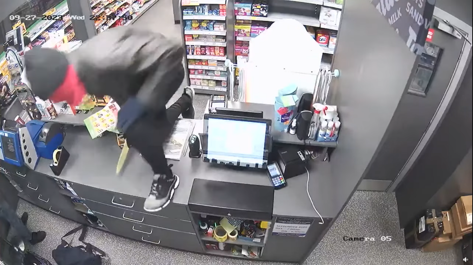 Man jumping over the counter in the store. He is covering his face and holding a knife