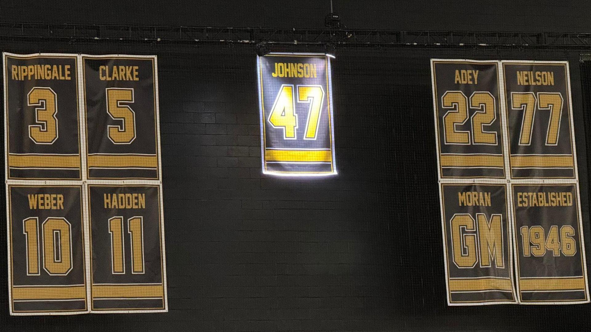 A sign to represent Adam Johnson's 47 Jersey hanging with the six other retired numbers by the club