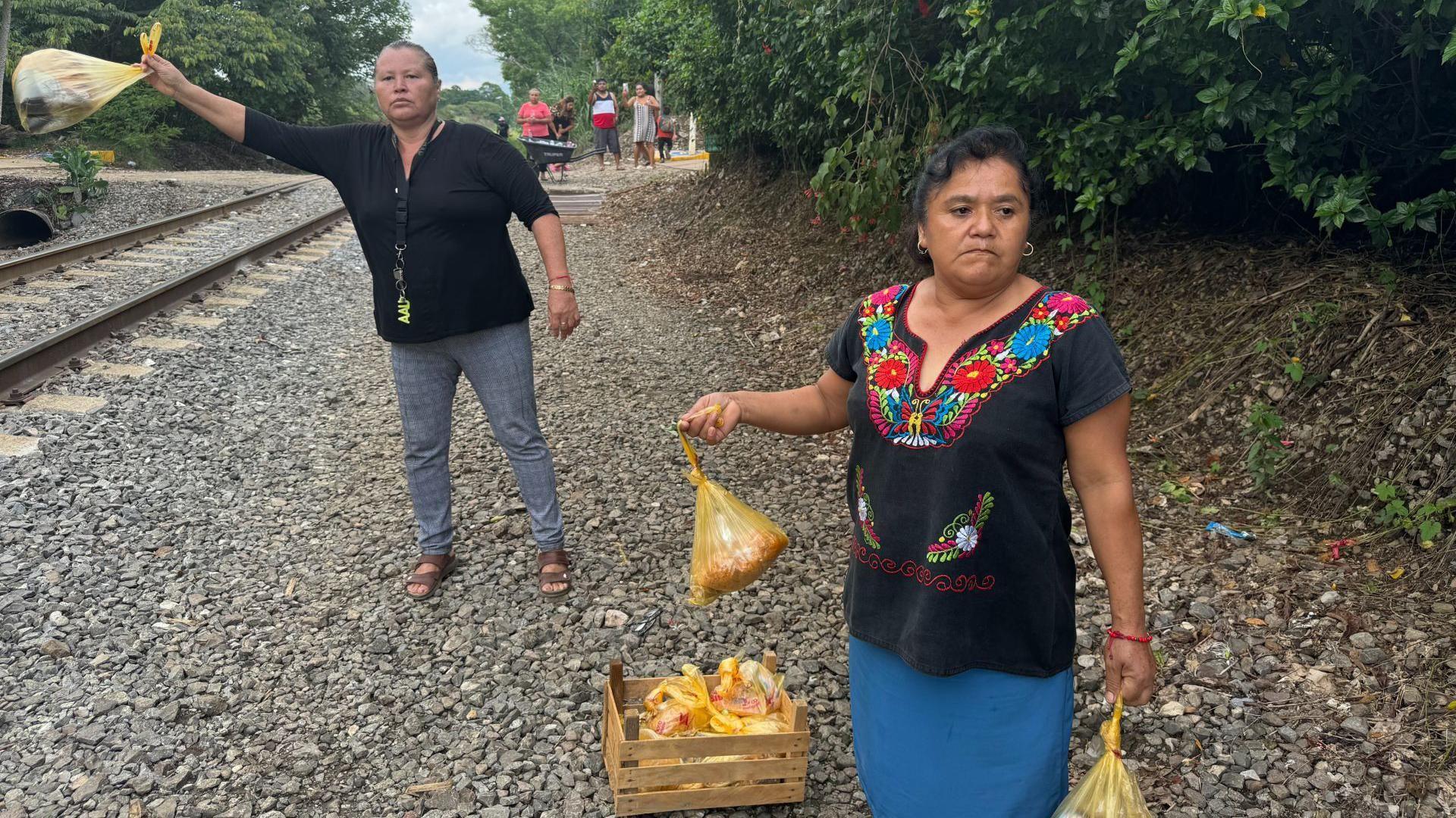 Members of Las Patronas hold out bags of food by the side of a railway track