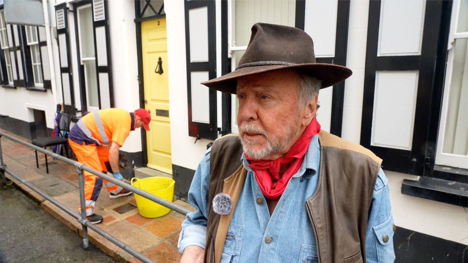 Man with hat in foreground while worker in background finishing installation of stone