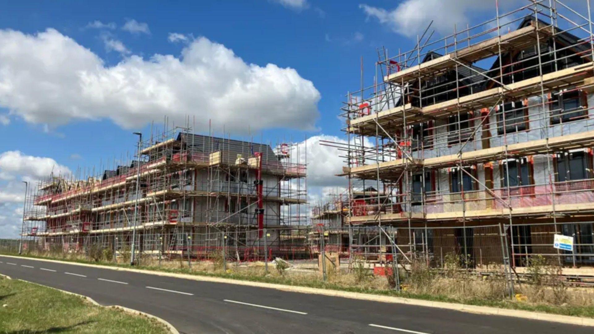 Three large partially built buildings with scaffolding around them and under construction. They are positioned beside a road.