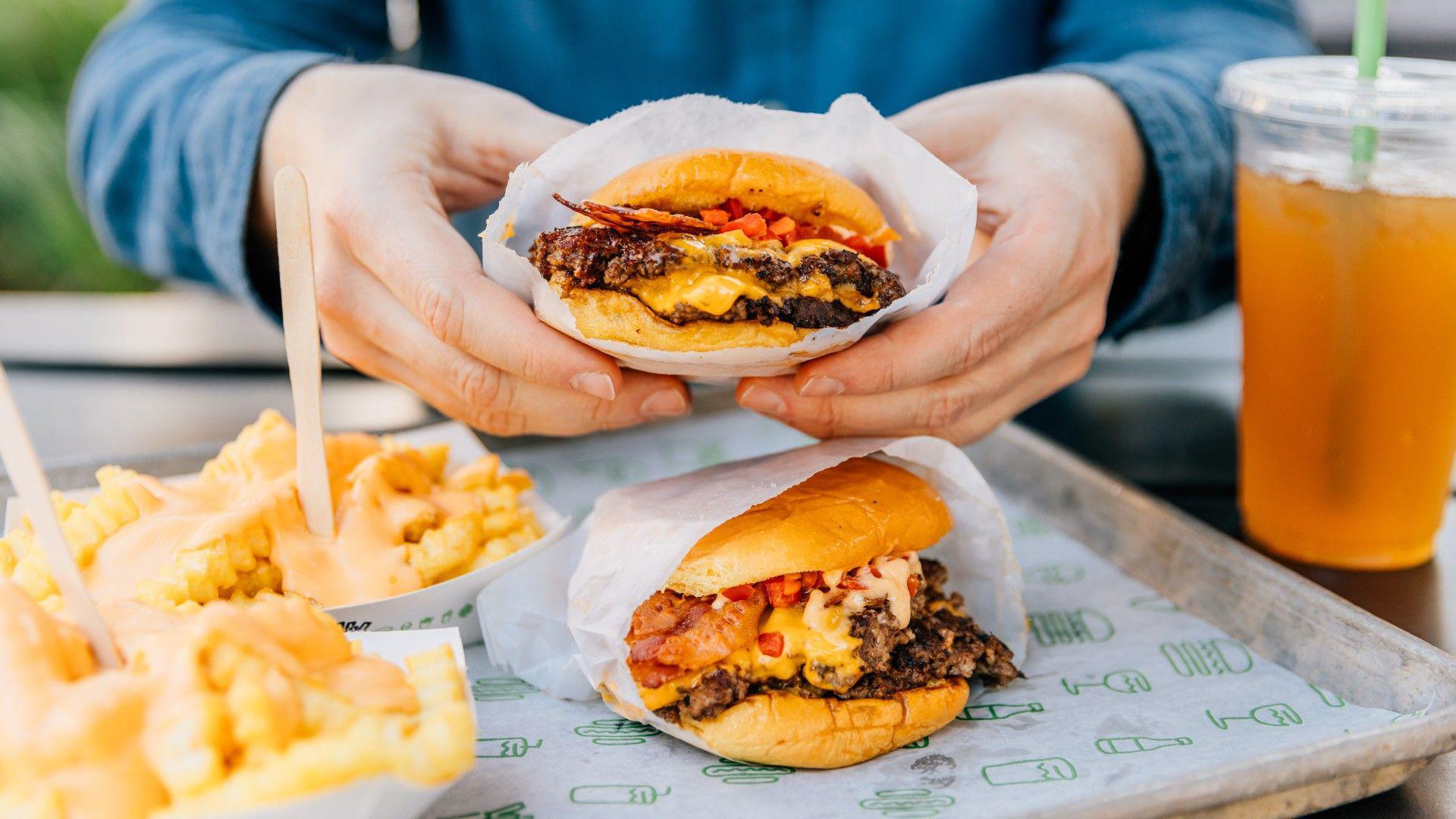 picture of two double cheeseburgers and two portions of chips with a drink 