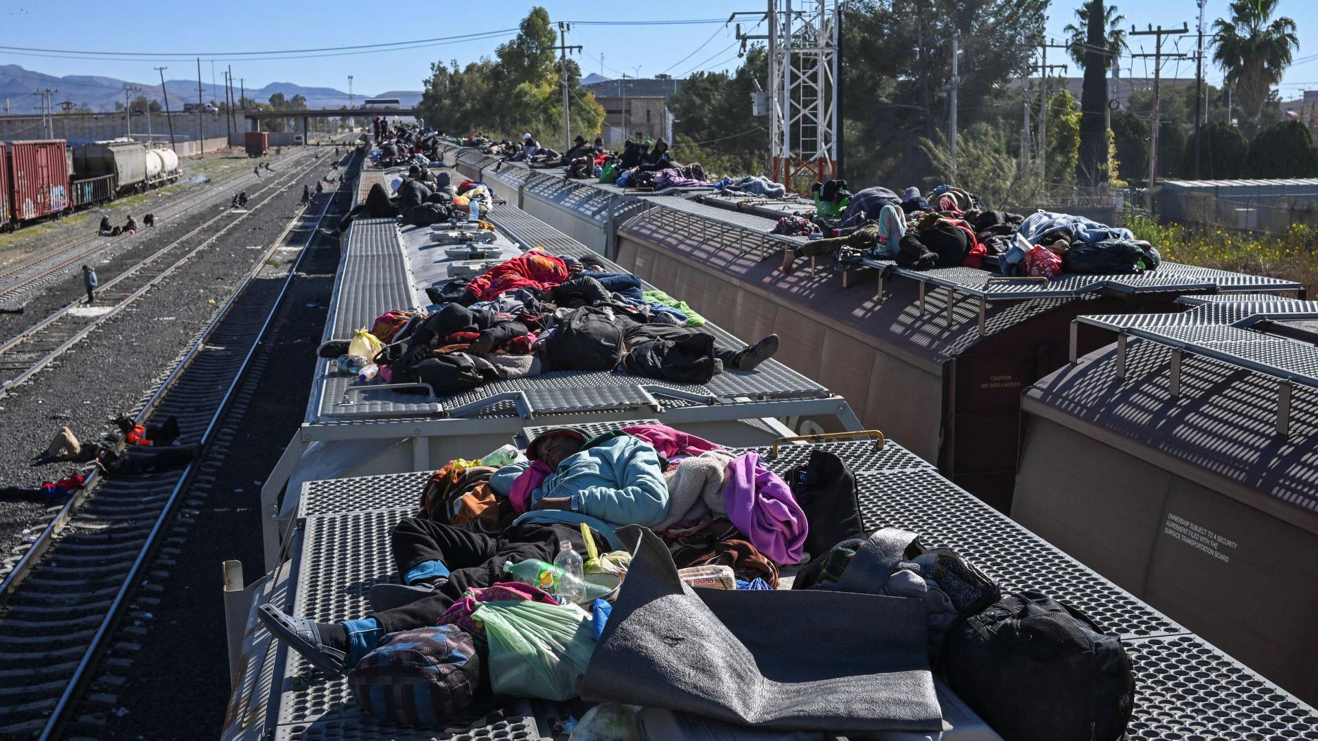 Migrants rest on railroad cars as they wait for a freight train to travel to the US border