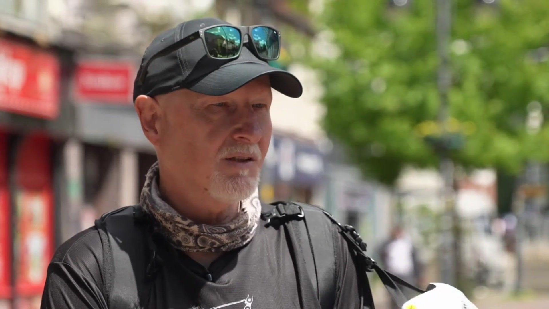 Gary Huett wearing a black baseball cap with sunglasses perched on top, a black T-shirt and a patterned scarf round his neck