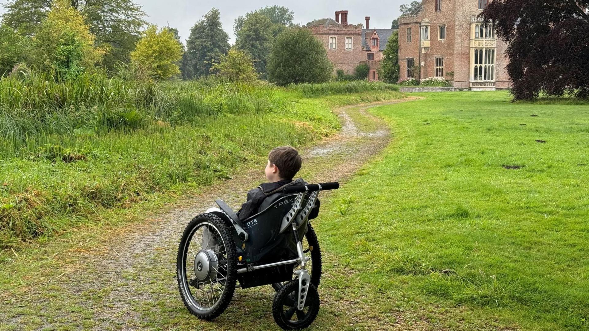 A young visitor using his all-terrain powerchair outside Oxburgh Estate