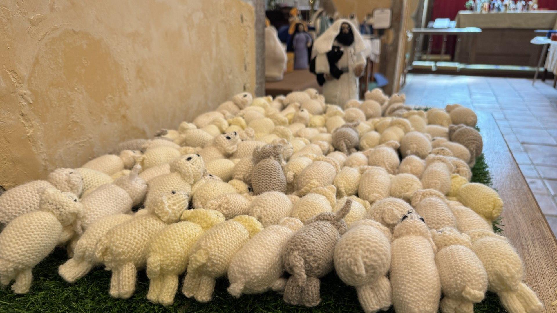 A knitted depiction of dozens of sheep being lead to safety by a shepherd.