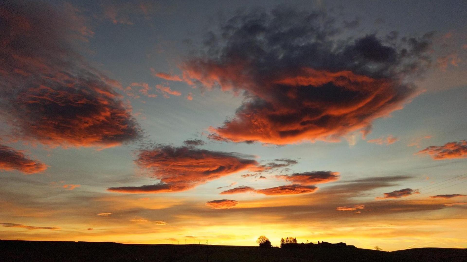 Fluffy clumps of red clouds over a rural landscape. The sky on the horizon is a dark yellow.