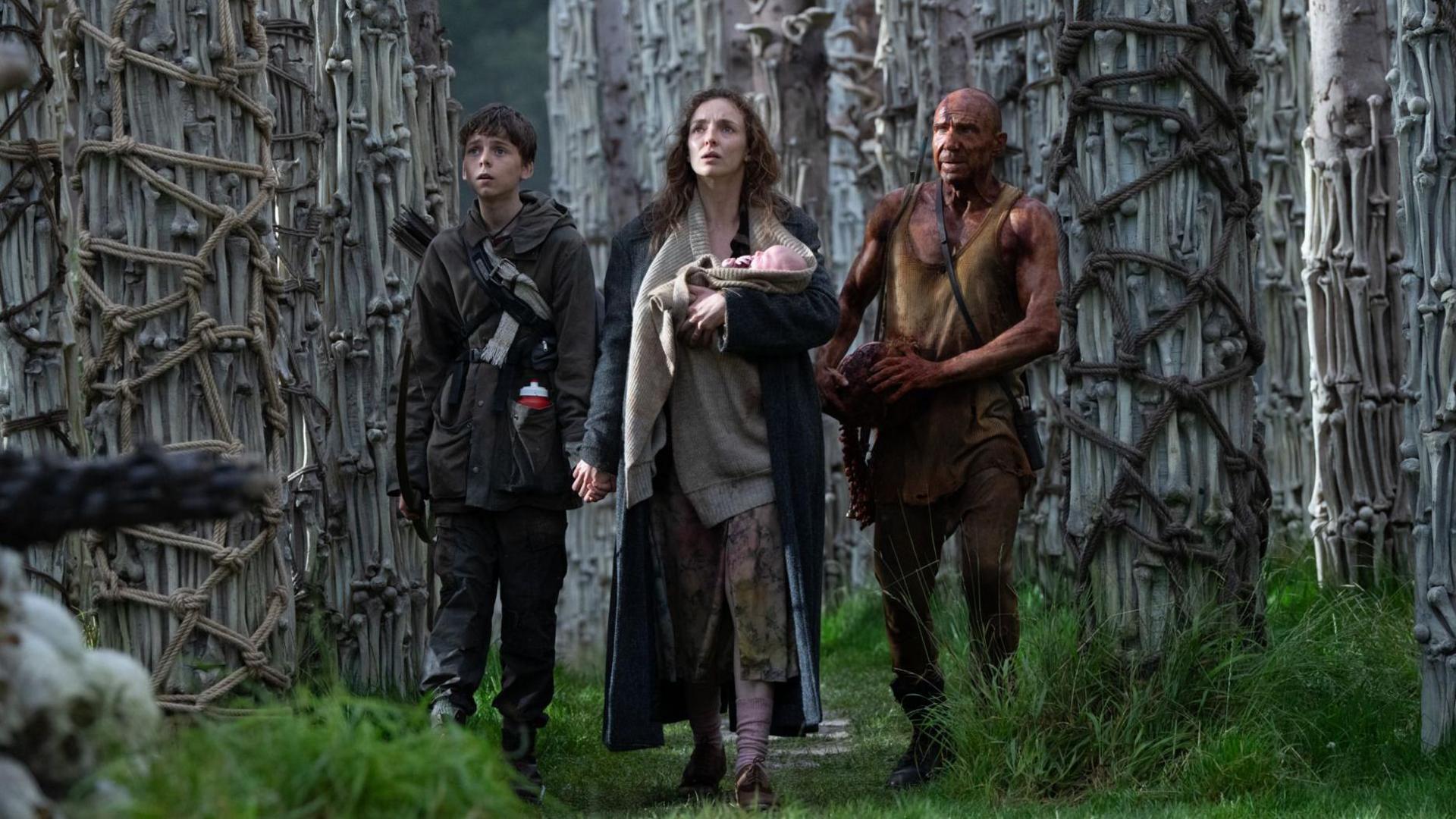 Spike, Jodie Comer holding a newborn, and Ralph Fiennes as Dr Kelson
