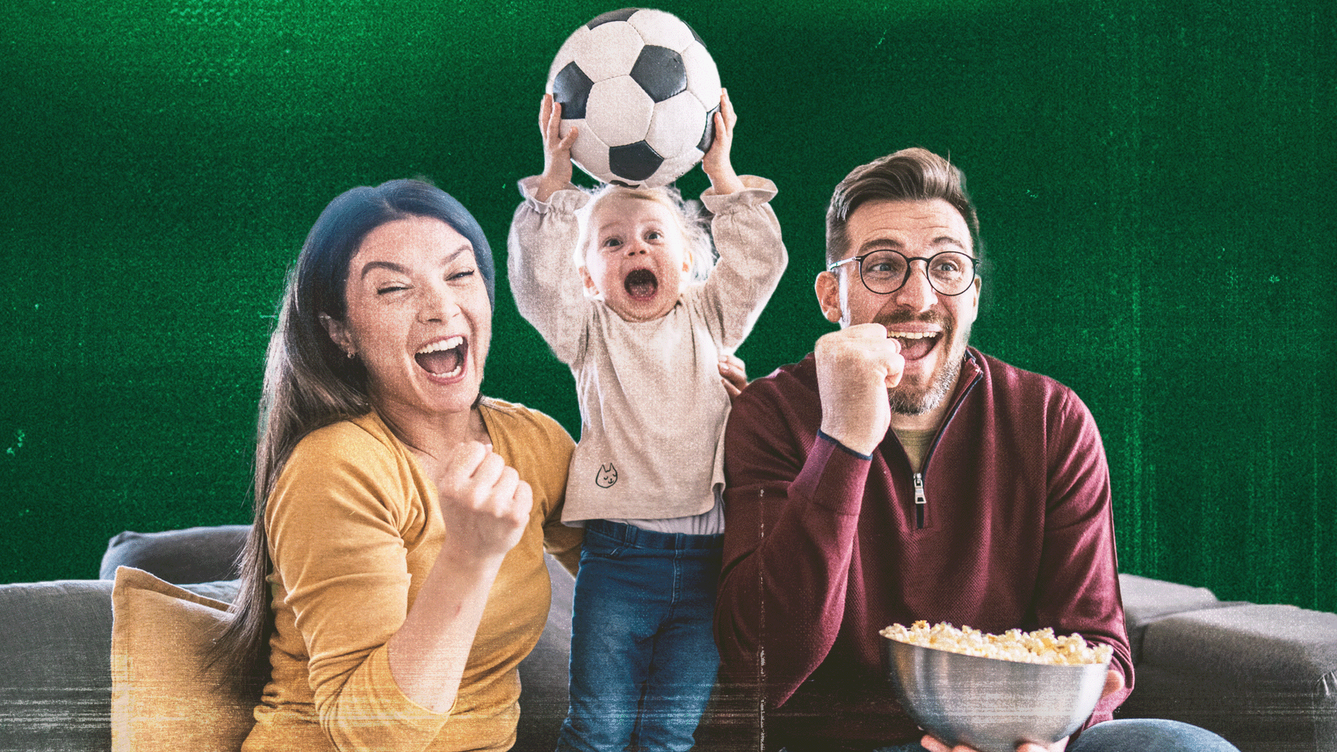 An image of a family on a sofa celebrating a goal in front of a dark green background. The family is made up of a women sitting on the left who is cheering and clenching her right fist in celebration. She has long dark hair and is wearing a yellow top. A young girl is standing in the middle, also cheering and holding a football above her head. She has fair hair, and is wearing a beige top and blue jeans. A man is sitting on the right, with short dark hair, a shaved beard and glasses. He is also clenching his right fist and cheering, while holding a bowl of popcorn in his left hand. He is wearing a red zipped jumper and blue jeans.