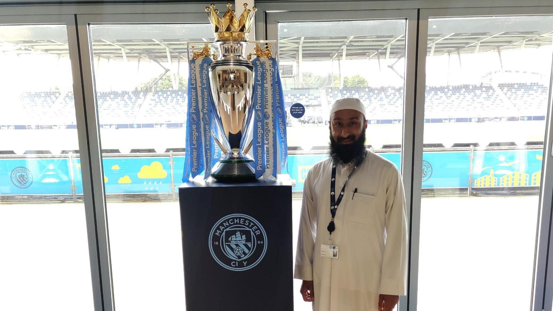 Imam Ismail Bhamji next to the Premier League trophy