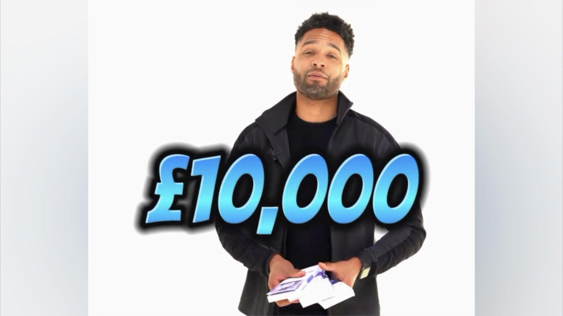 Mr Hall, who has short, cropped dark hair and short shaved facial hair. He is wearing a black jacket with grey jeans and holding money. A piece a text stretching across the screen says £10,000 in advert of a competition