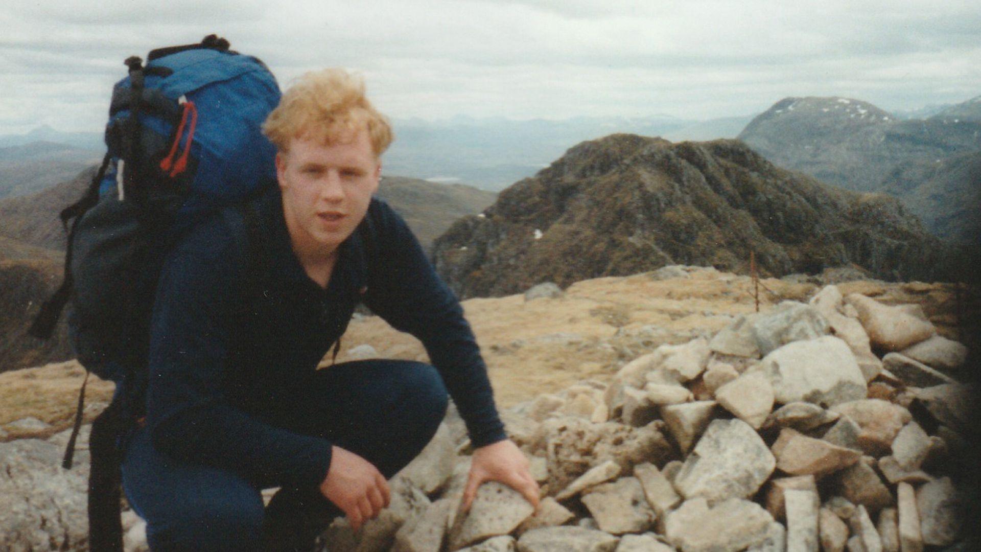 A photo of Rob on a hilltop. He is wearign dark blue clothing and is carrying a backpack