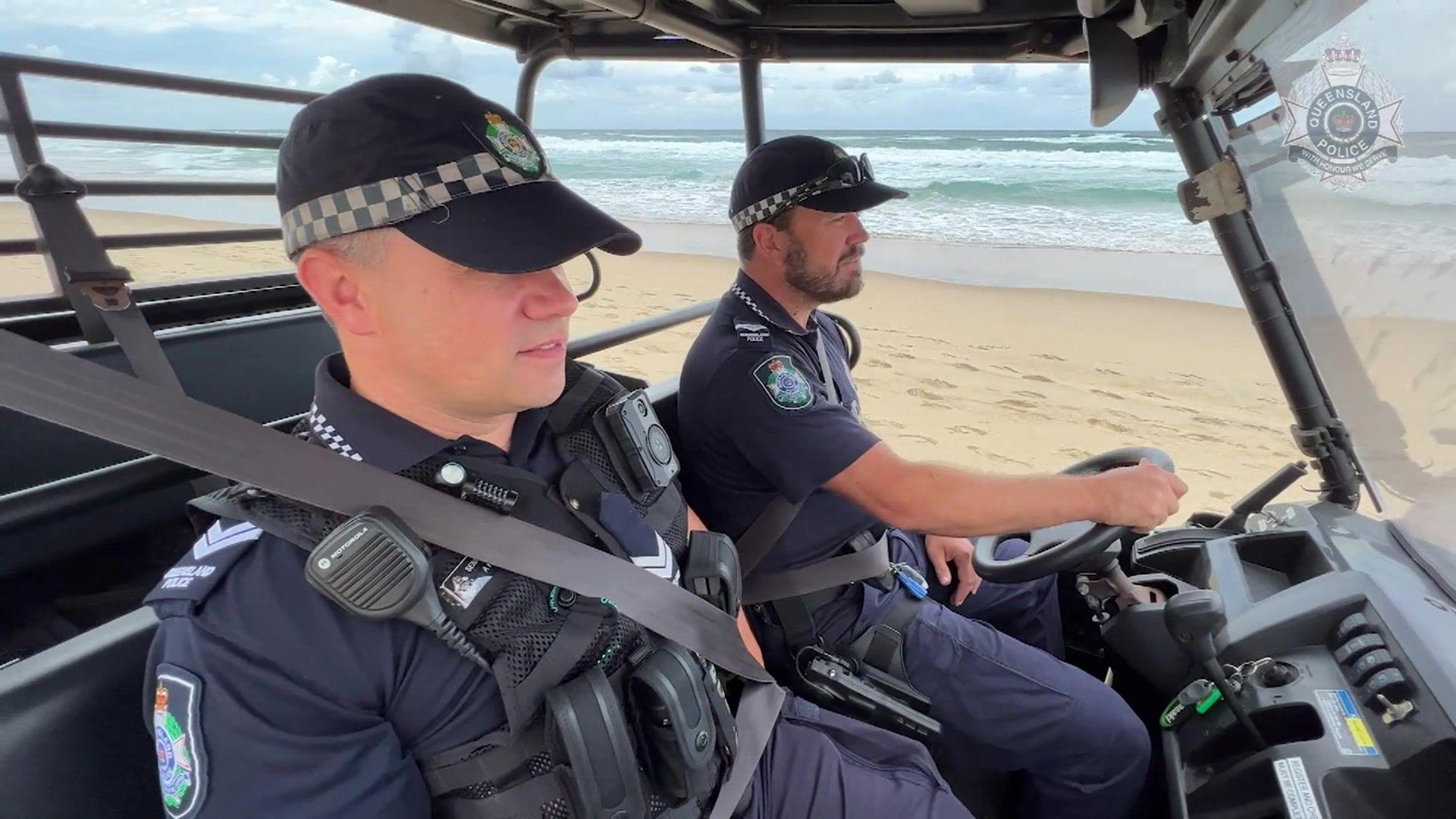 Two police officers sit inside a sand buggy driving on a beach