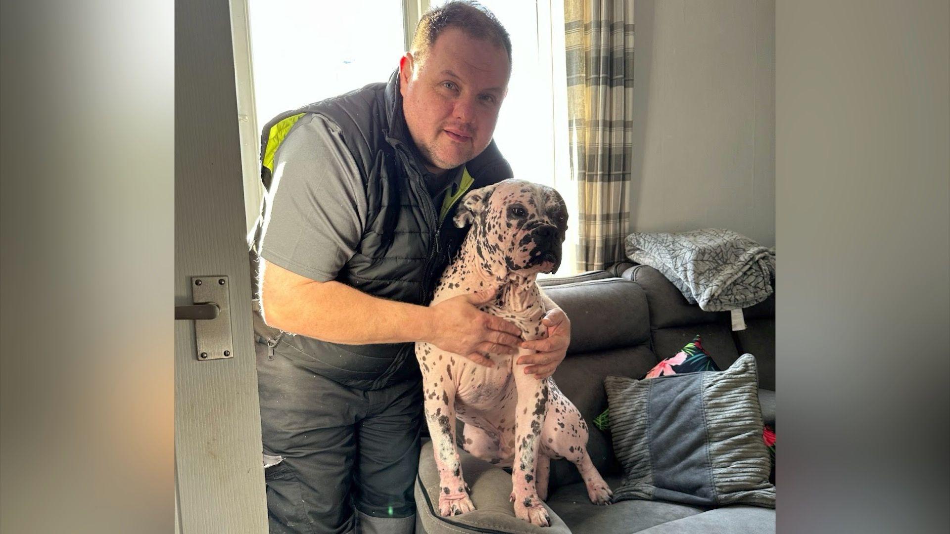 Patch sat on the arm of a grey sofa with his owner's arms around him.