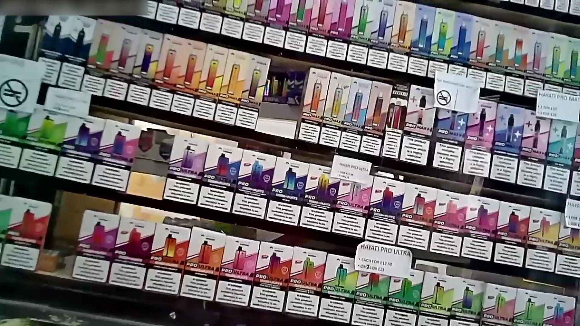 A selection of colourful vapes shelves behind a shop counter.